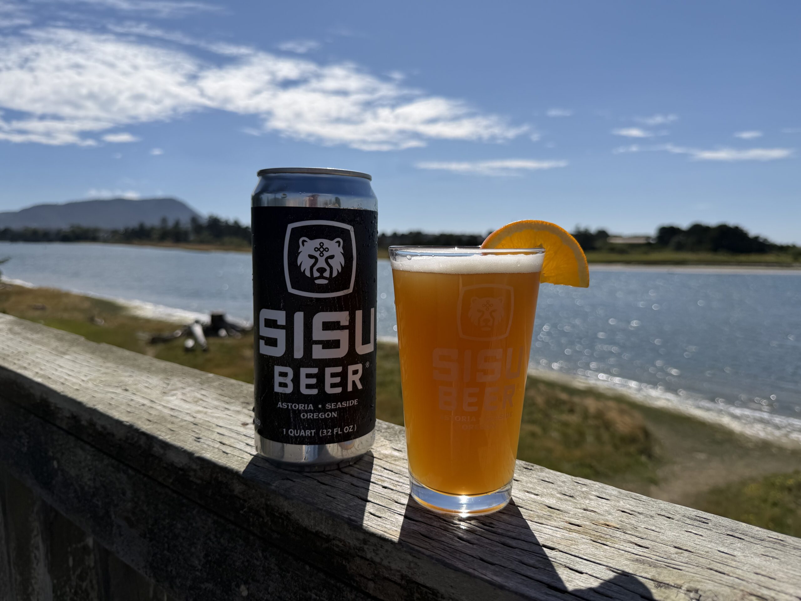 Sisu Beer 32 oz can and branded pint glass with an orange slice on the Seaside waterfront