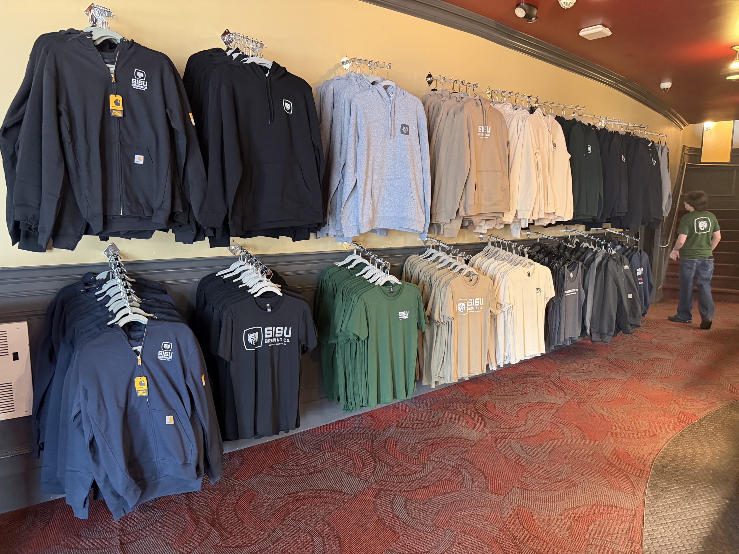 Sisu Brewing Co merch wall Sisu Brewing Co merch wall at the Times Theater — hoodies, t-shirts, and tank tops on display